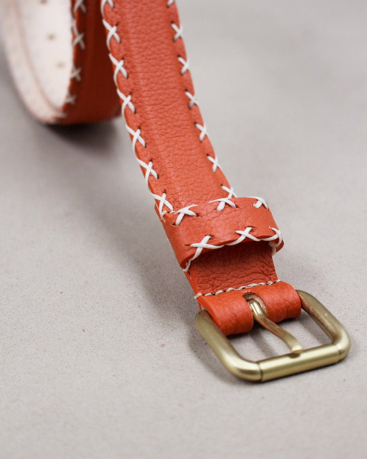 Gros plan boucle carrée dorée sur ceinture cuir orange à surpiqûres croisées Berthille
