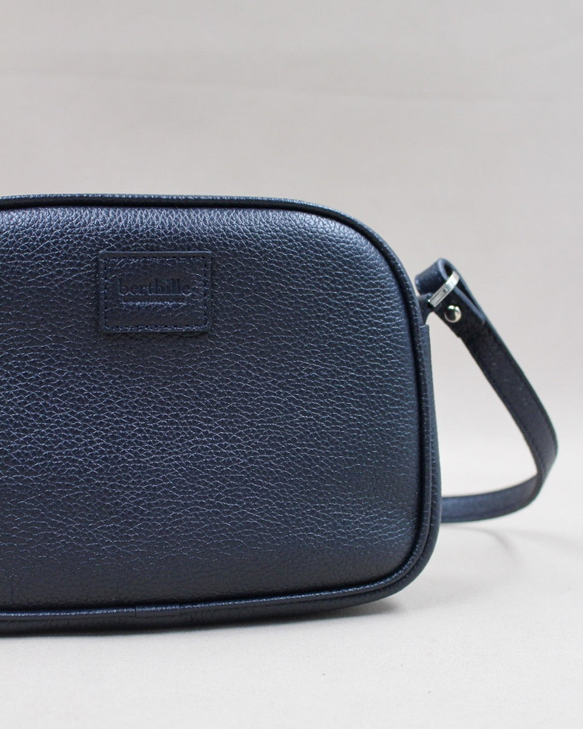 Gros plan logo gravé et bandoulière, minaudière cuir grainé bleu marine Berthille