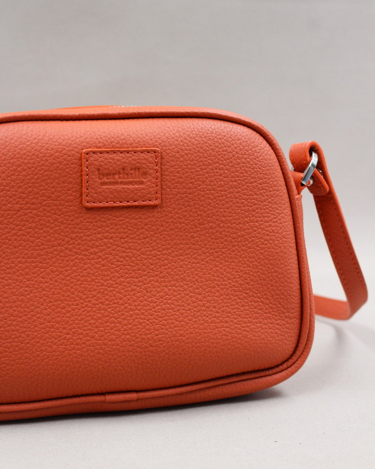 Gros plan logo gravé et bandoulière, minaudière cuir grainé orange Berthille