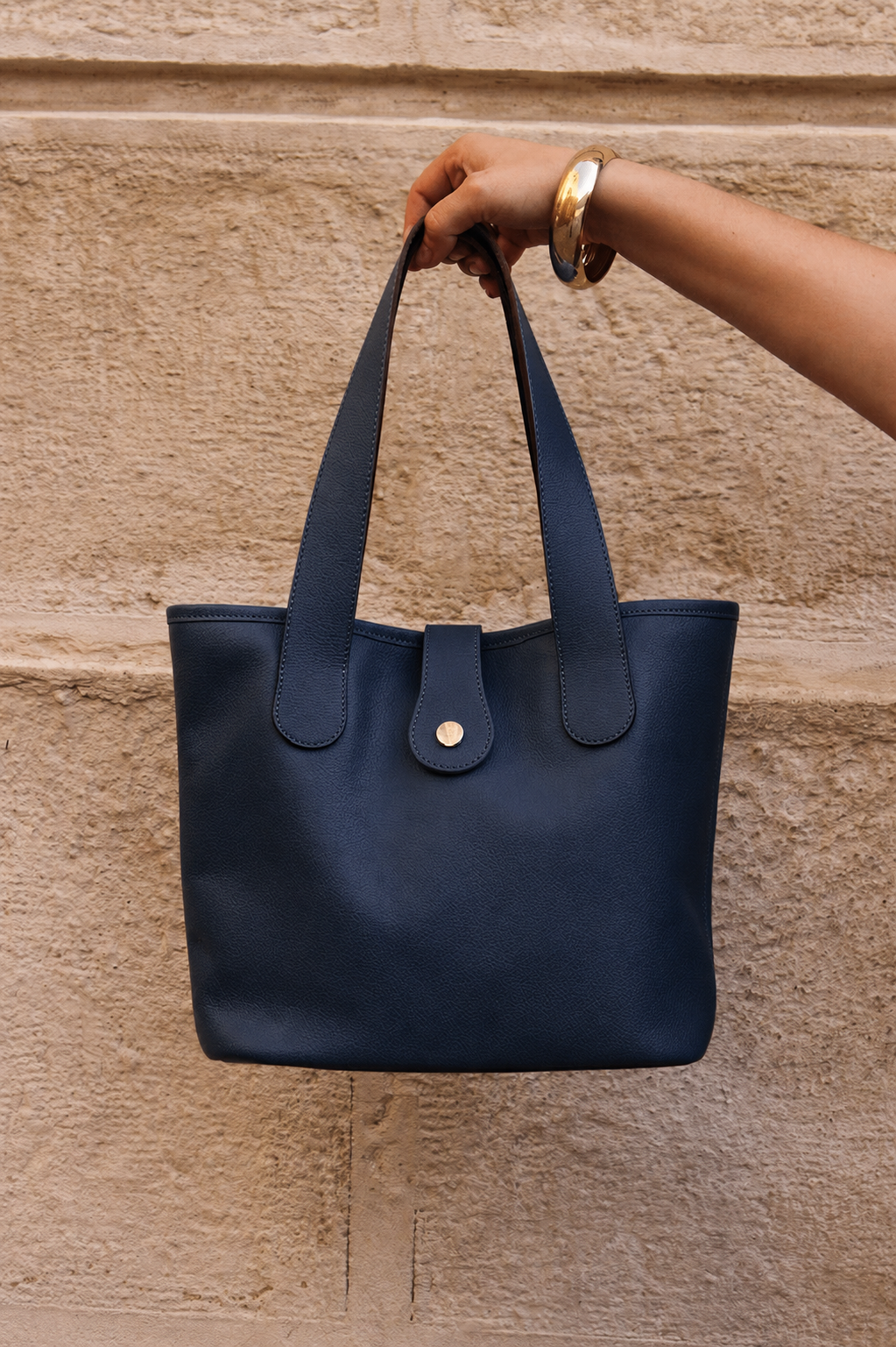 Sac berthille bleu marine en cuir de vachette pleine fleur sur un mur en pierre beige 