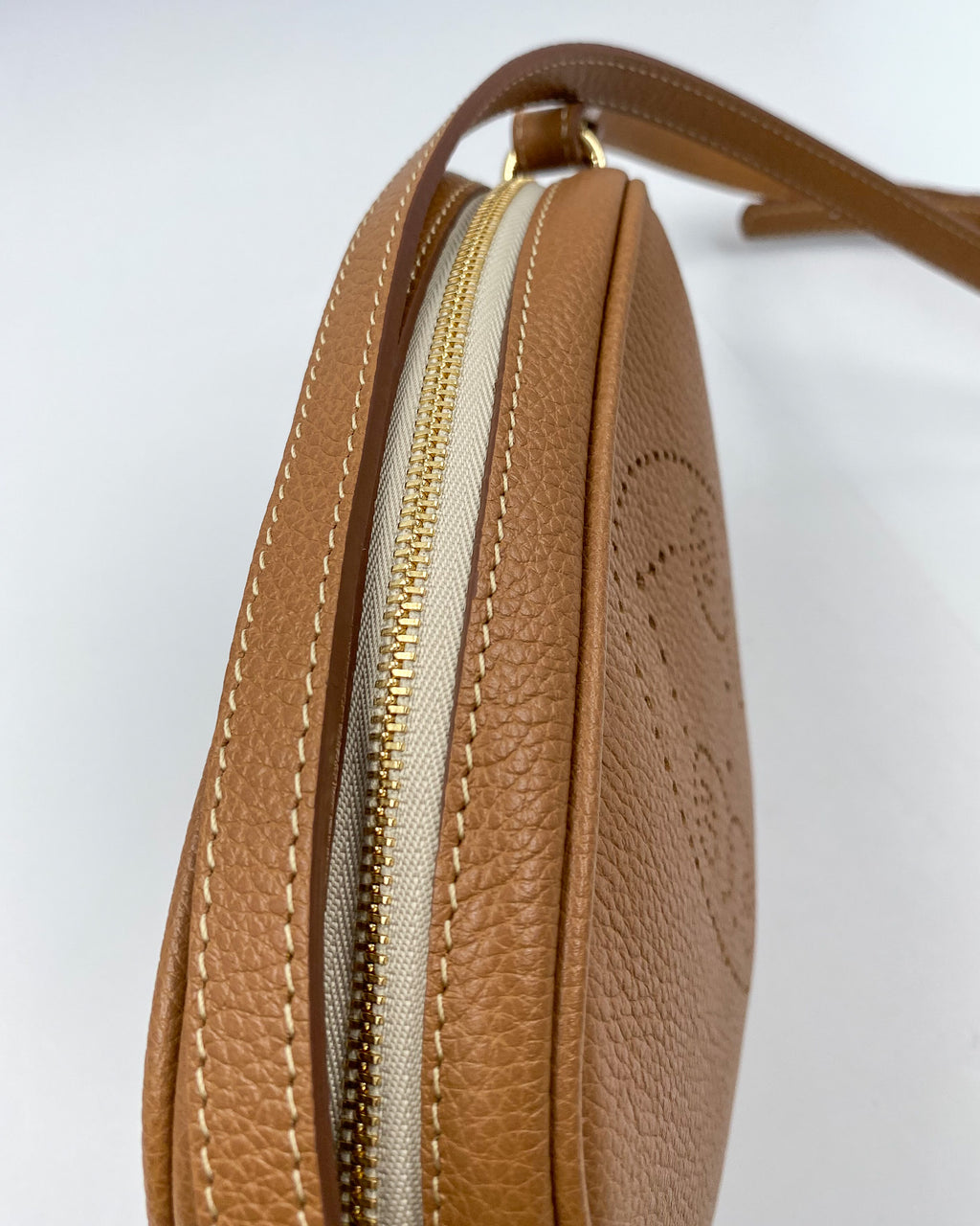 Détail de la pochette Trianon en cuir camel : fermeture éclair dorée, coutures sellier et bandoulière en cuir, fabrication artisanale française