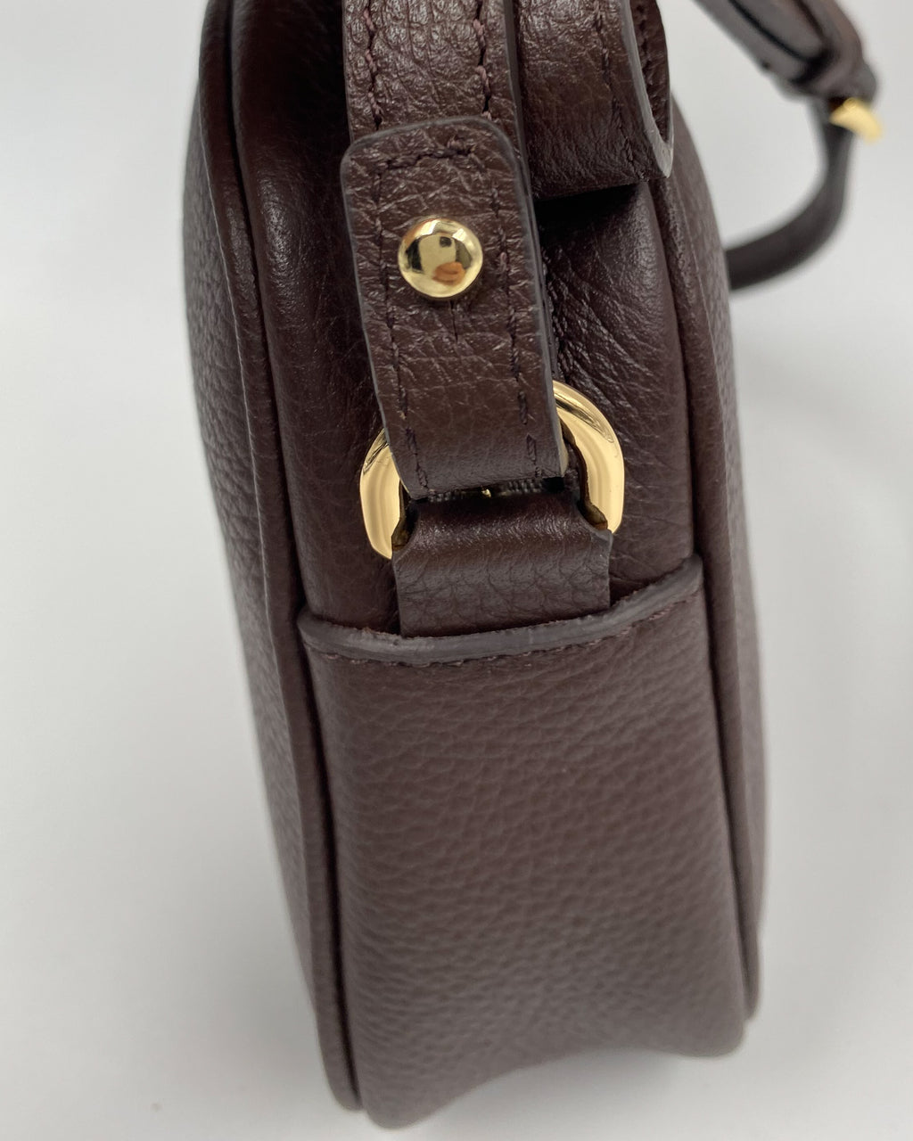 Vue de côté de la pochette Trianon en cuir chocolat grainé, attache de bandoulière avec bouton et anneau dorés, fabrication artisanale française