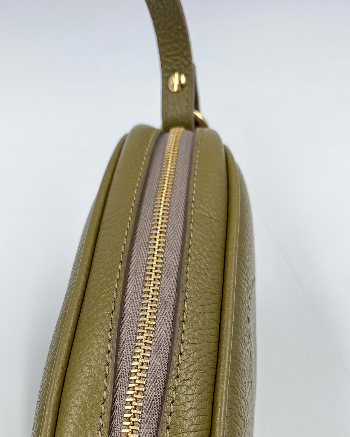 Vue du dessus de la pochette Trianon en cuir kaki grainé, fermeture éclair dorée et coutures ton sur ton, fabrication artisanale française