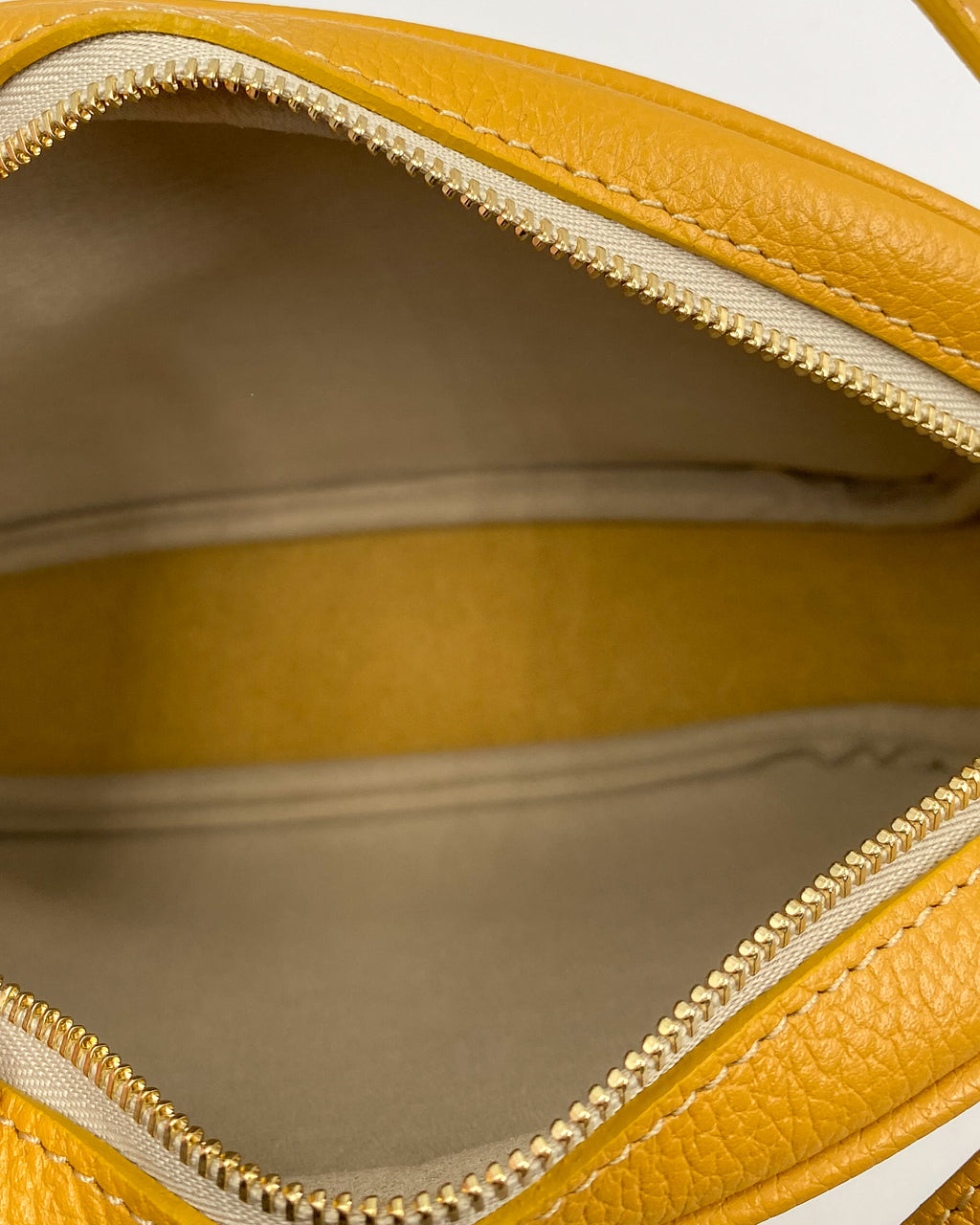 Intérieur de la pochette Trianon en cuir jaune moutarde : doublure beige, deux compartiments et fermeture éclair dorée