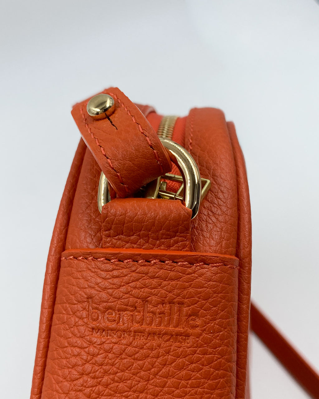 Détail de la pochette Trianon en cuir orange : logo Berthille Maison Française embossé, attache de bandoulière et anneau dorés