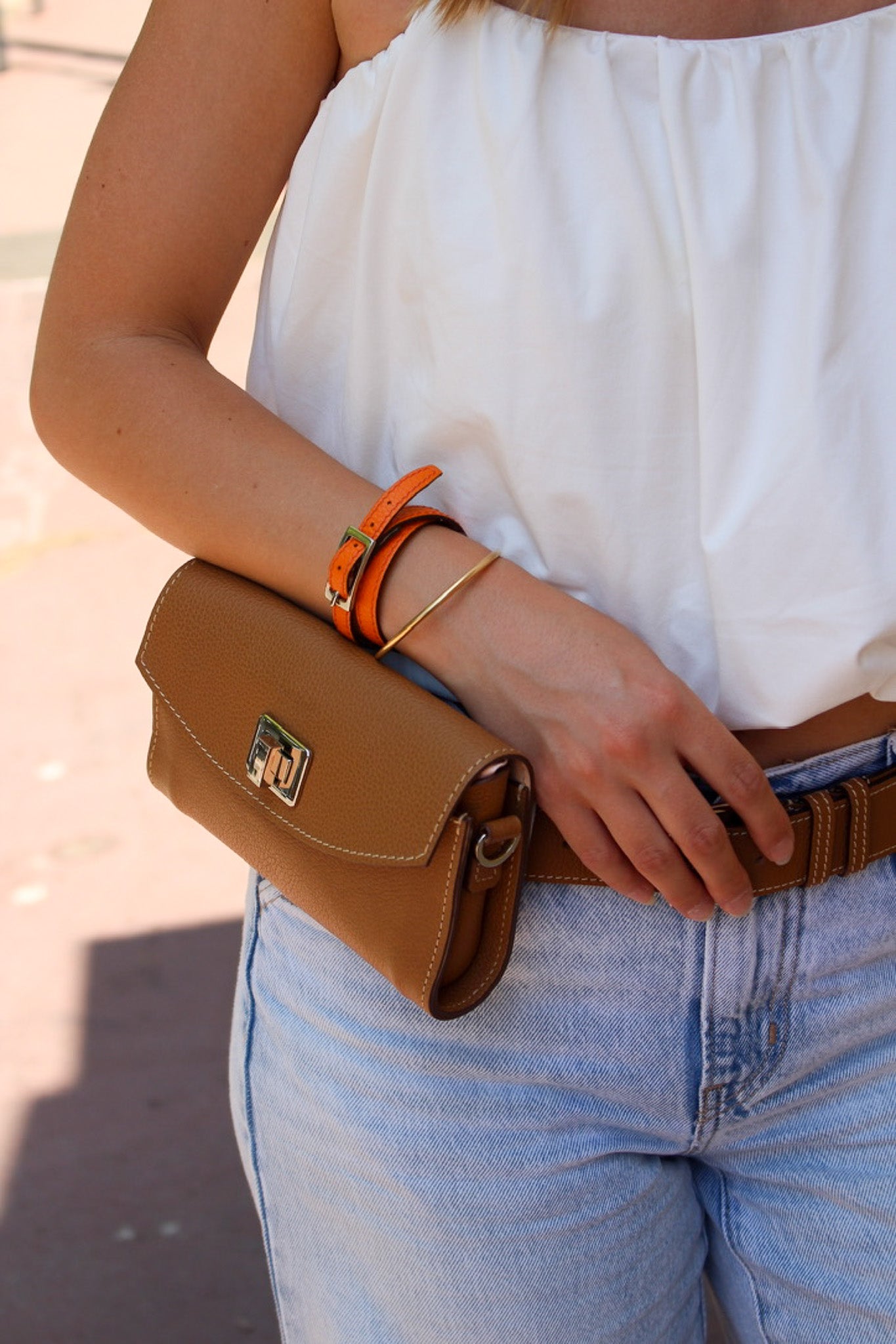 Pochette cuir en couleur caramel porter autour d'une ceinture par une femme avec un bracelet orange 