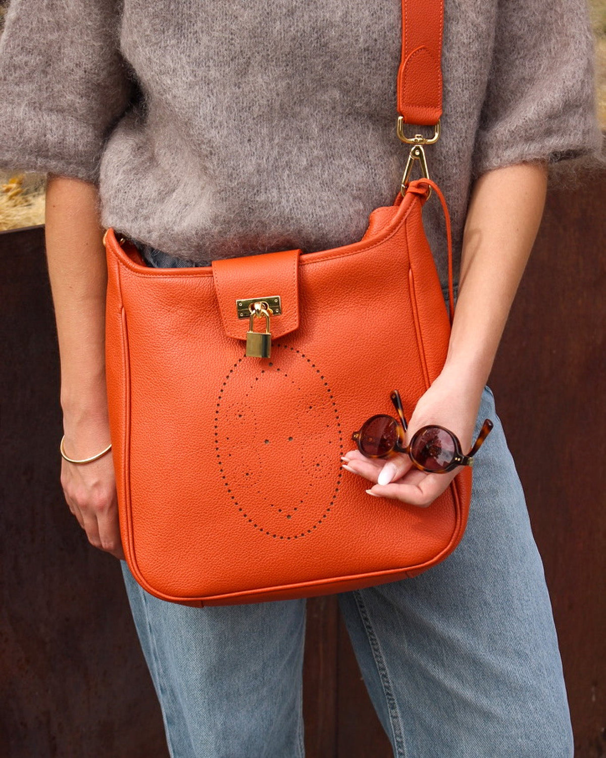 Sac en cuir Rivoli coloris orange porter en bandoulière par une femme avec des lunette de soleil