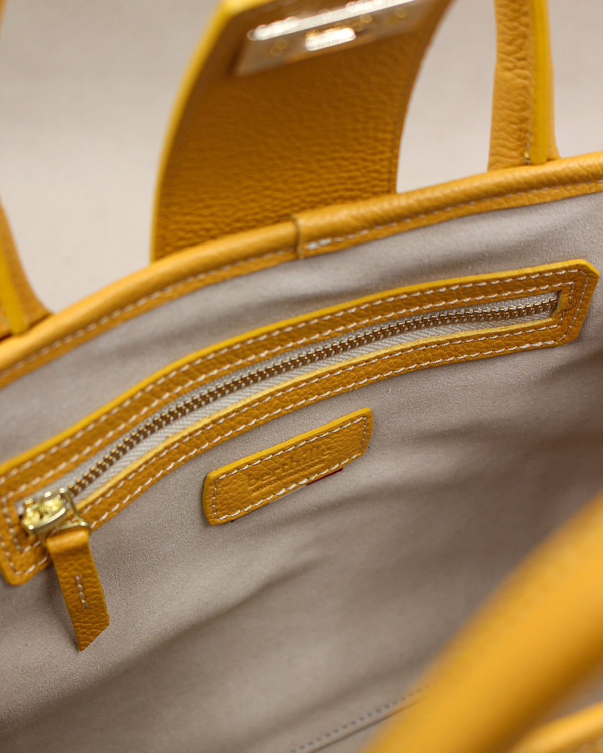 Détail intérieur du sac à main Mini Vendôme en cuir jaune moutarde : poche zippée bordée de cuir surpiqué, tirette en cuir et doublure gris clair, fabrication artisanale française