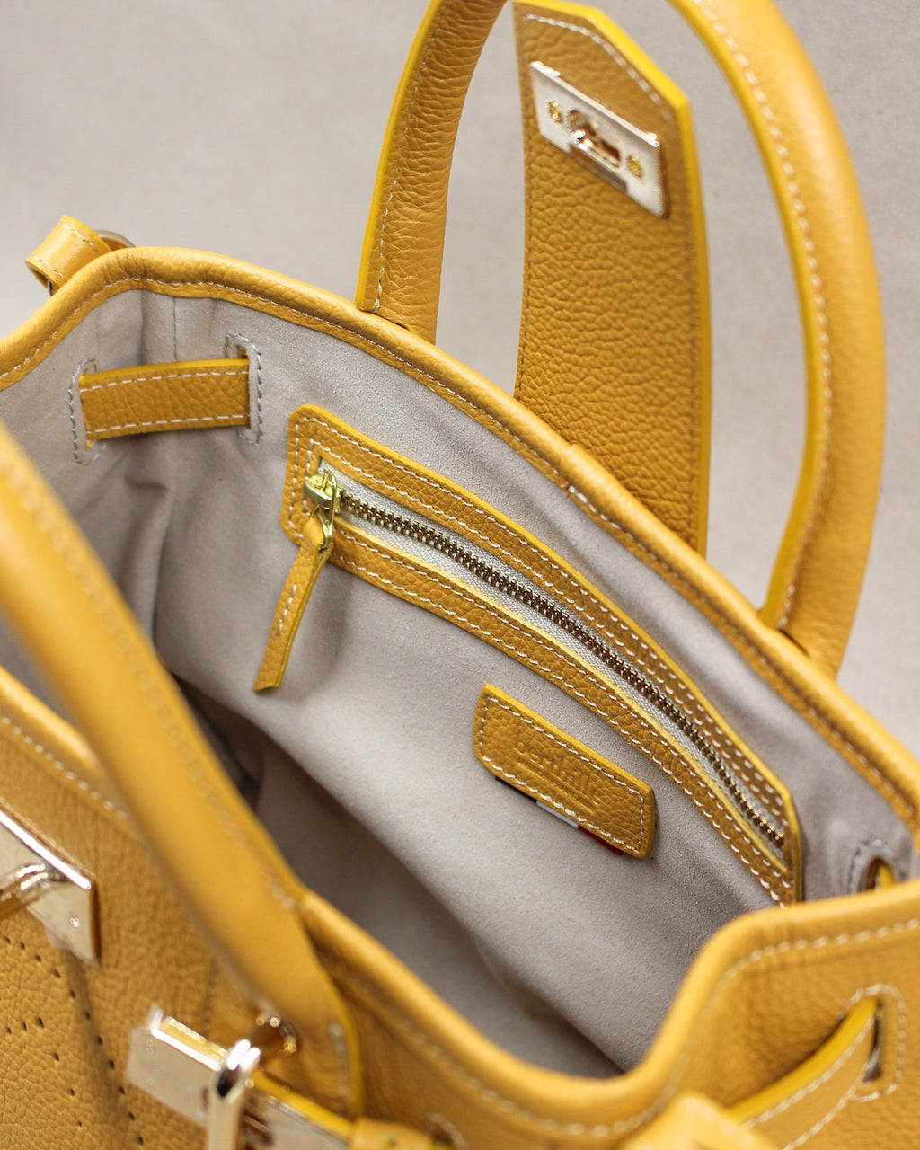 Intérieur du sac à main mini vendome en cuir jaune moutarde : doublure gris clair, poche zippée bordée de cuir et étiquette en cuir Berthille
