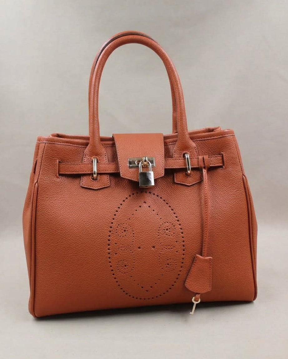 Sac à main Vendôme en cuir cognac vue de trois quarts, motif perforé bout fleuri, deux anses, sangle ceinturée, cadenas argenté, clé et clochette en cuir, fabriqué en France par Berthille