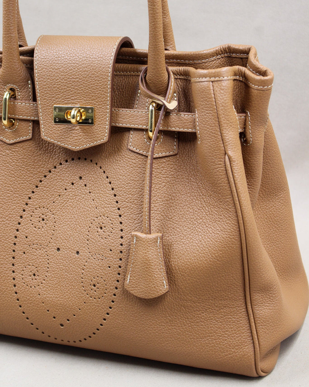 Sac à main Vendôme en cuir camel vue de trois quarts, motif perforé bout fleuri, sangle ceinturée, fermoir tournant doré, clochette en cuir et soufflets latéraux, maroquinerie artisanale française