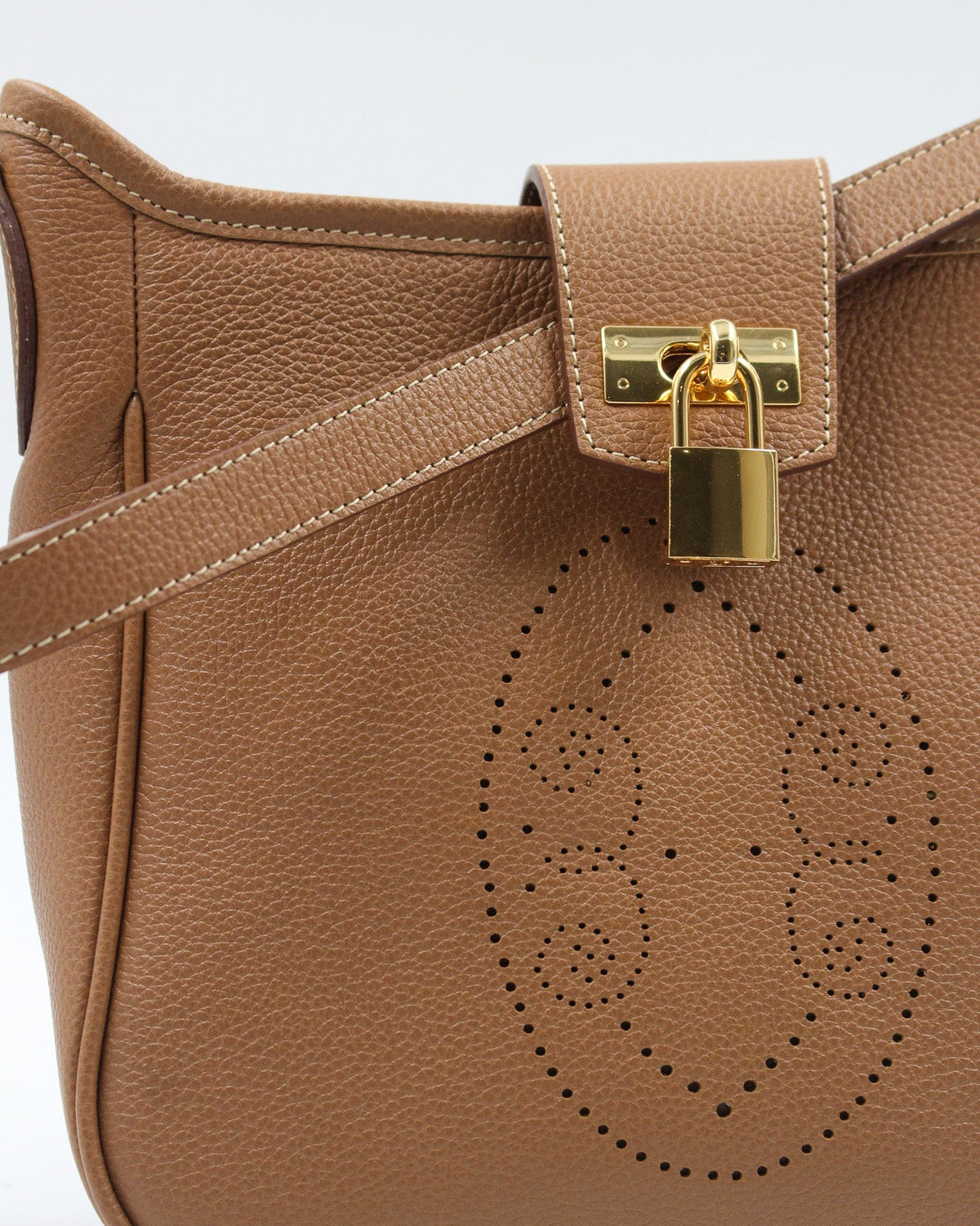 Gros plan sur le motif perforé bout fleuri du sac Trianon en cuir camel grainé, cadenas doré et coutures sellier, savoir-faire artisanal français