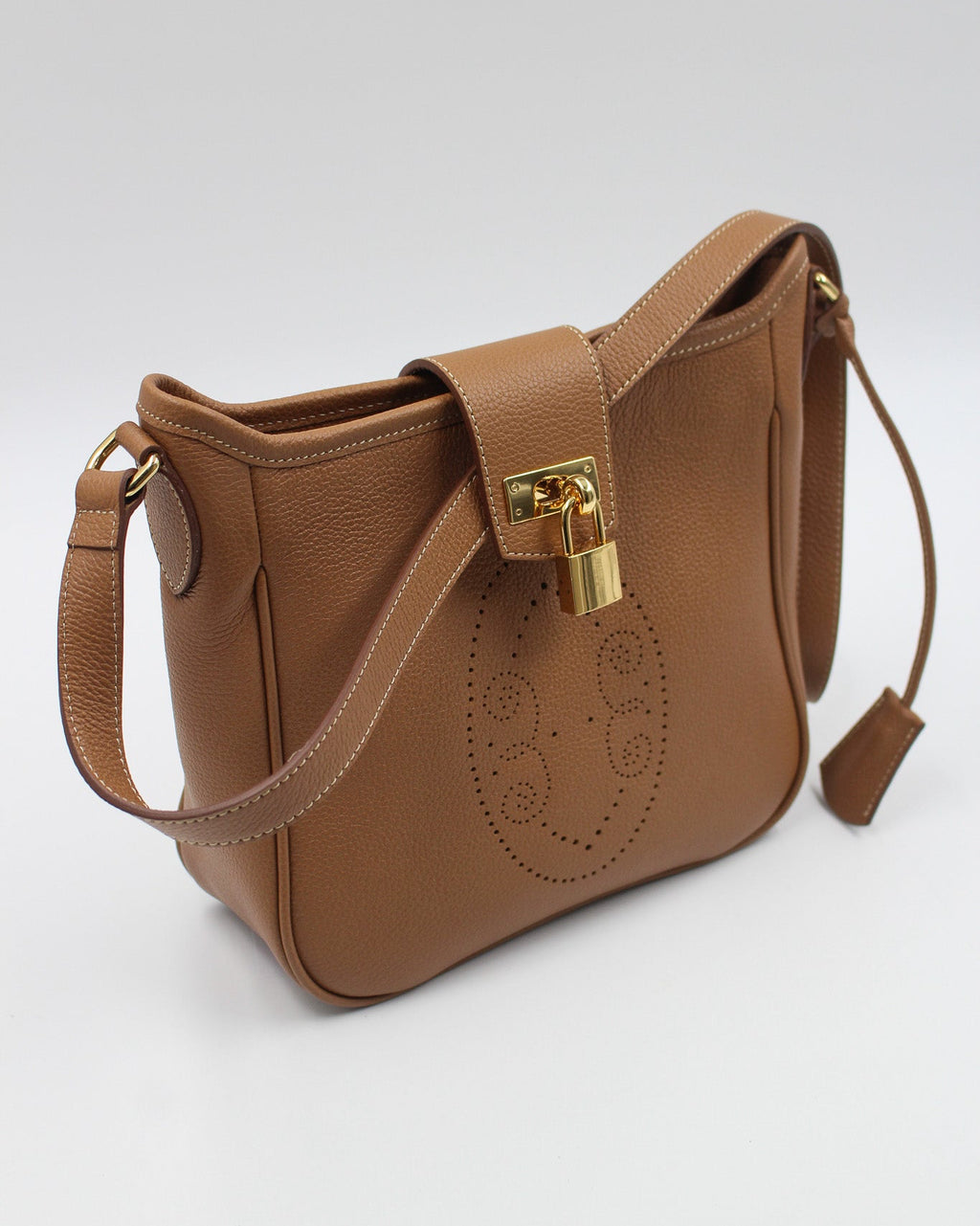 Sac Trianon en cuir camel vue de trois quarts, motif perforé bout fleuri, cadenas doré et clochette en cuir, maroquinerie artisanale française