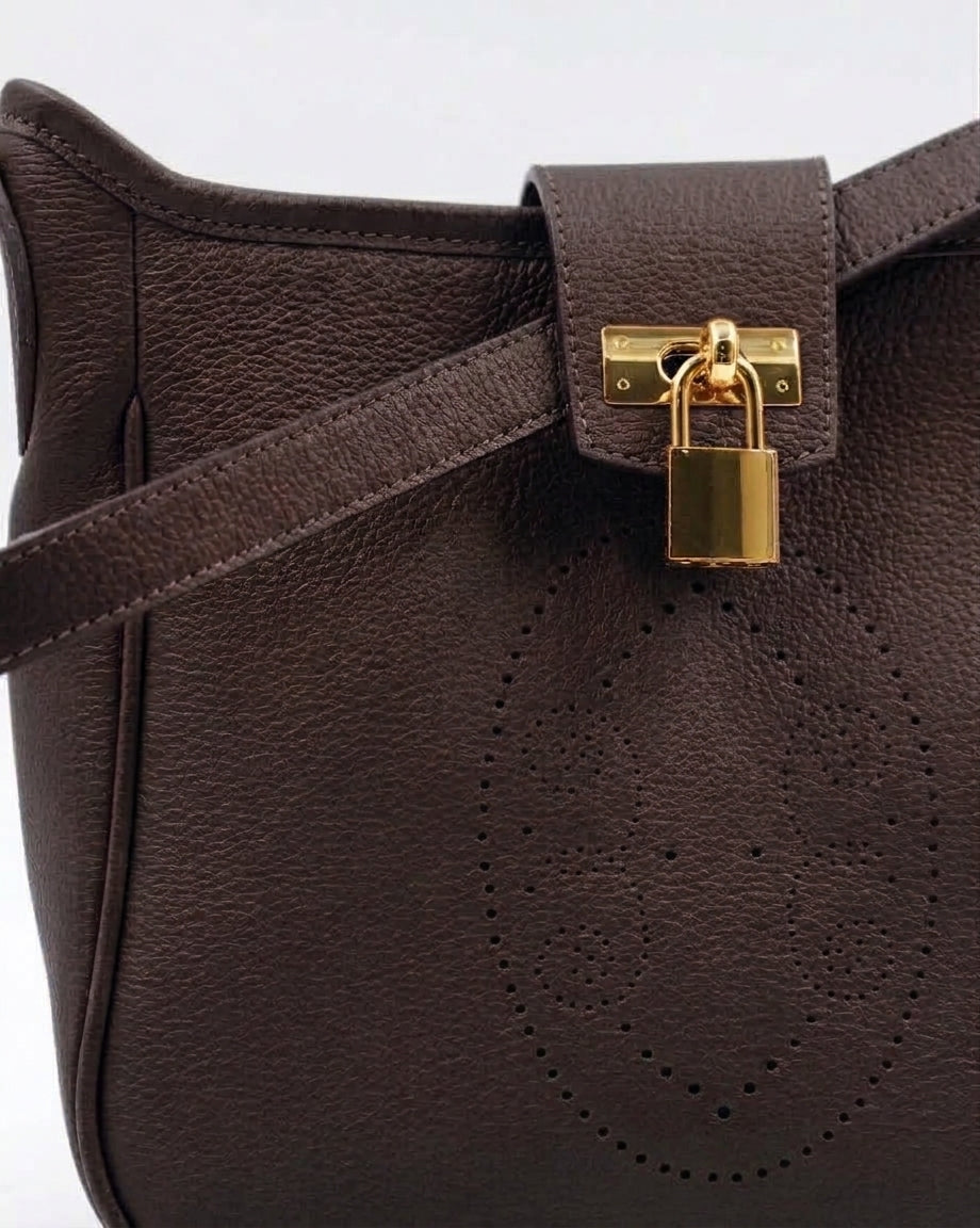 Gros plan sur le motif perforé bout fleuri du sac Trianon en cuir chocolat grainé, cadenas doré et coutures ton sur ton, savoir-faire artisanal français