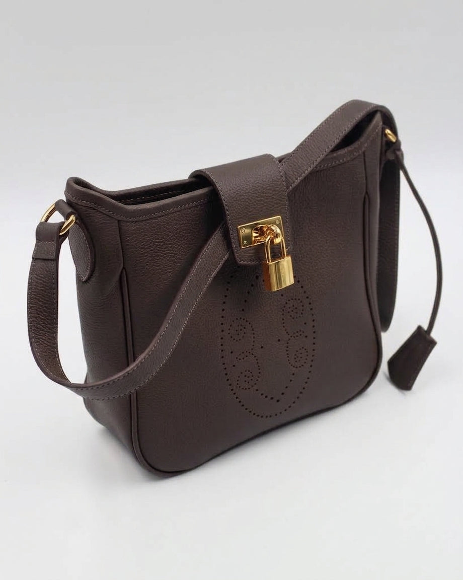 Sac Trianon en cuir chocolat vue de trois quarts, motif perforé bout fleuri, cadenas doré et clochette en cuir, maroquinerie artisanale française