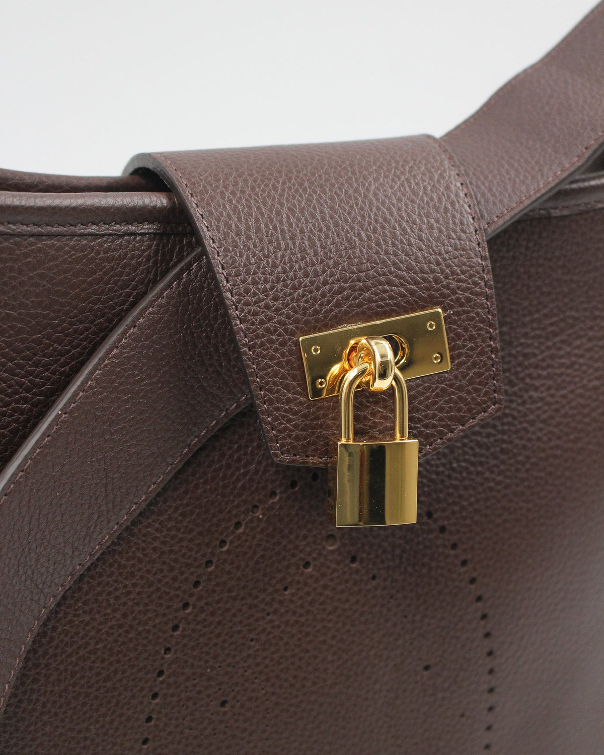 Détail du sac Trianon grand format en cuir chocolat grainé : rabat, fermoir et cadenas dorés, début du motif perforé bout fleuri, fabrication artisanale française