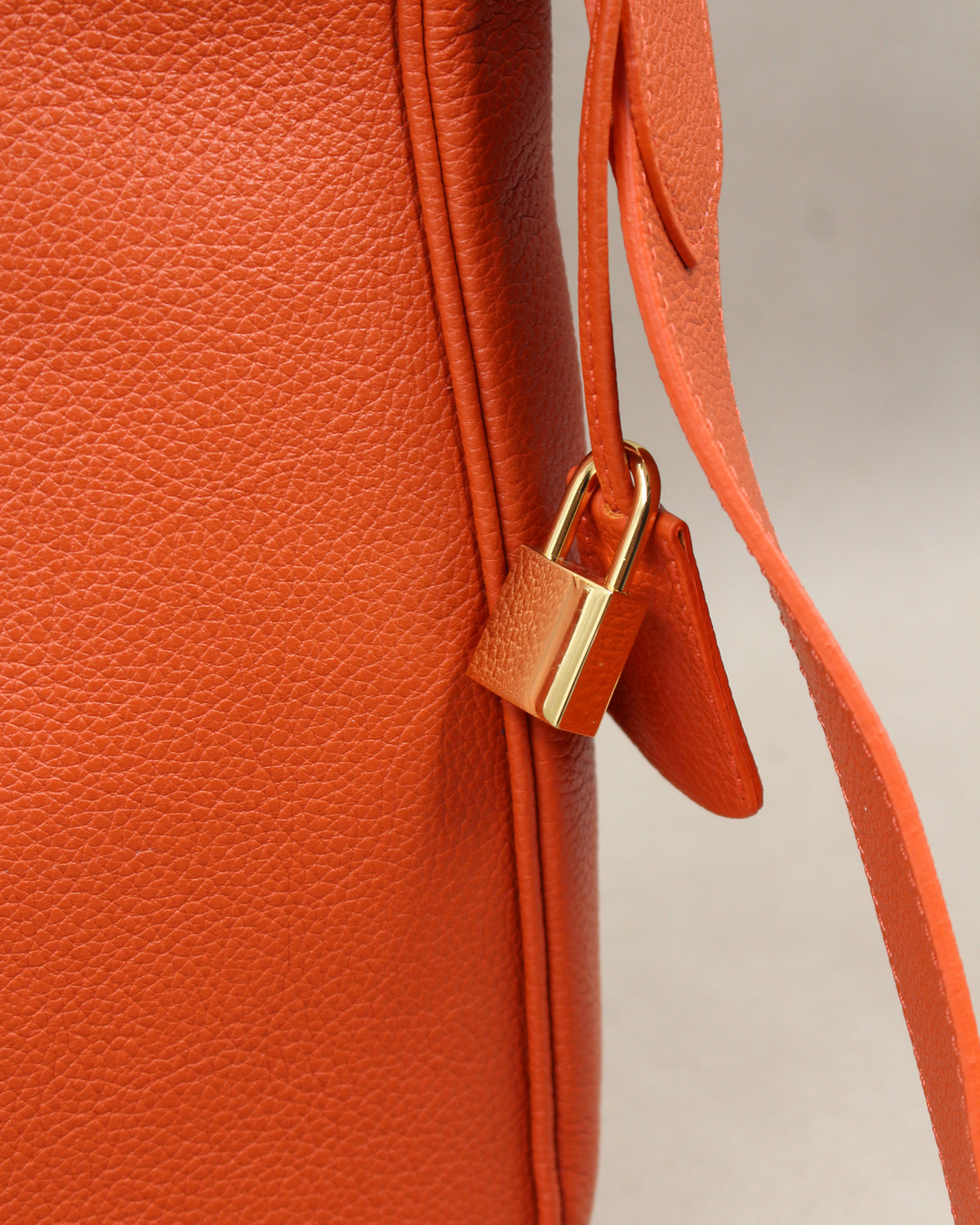 Détail du sac Trianon grand format en cuir orange grainé : cadenas doré et clochette en cuir suspendus à la bandoulière, fabrication artisanale française