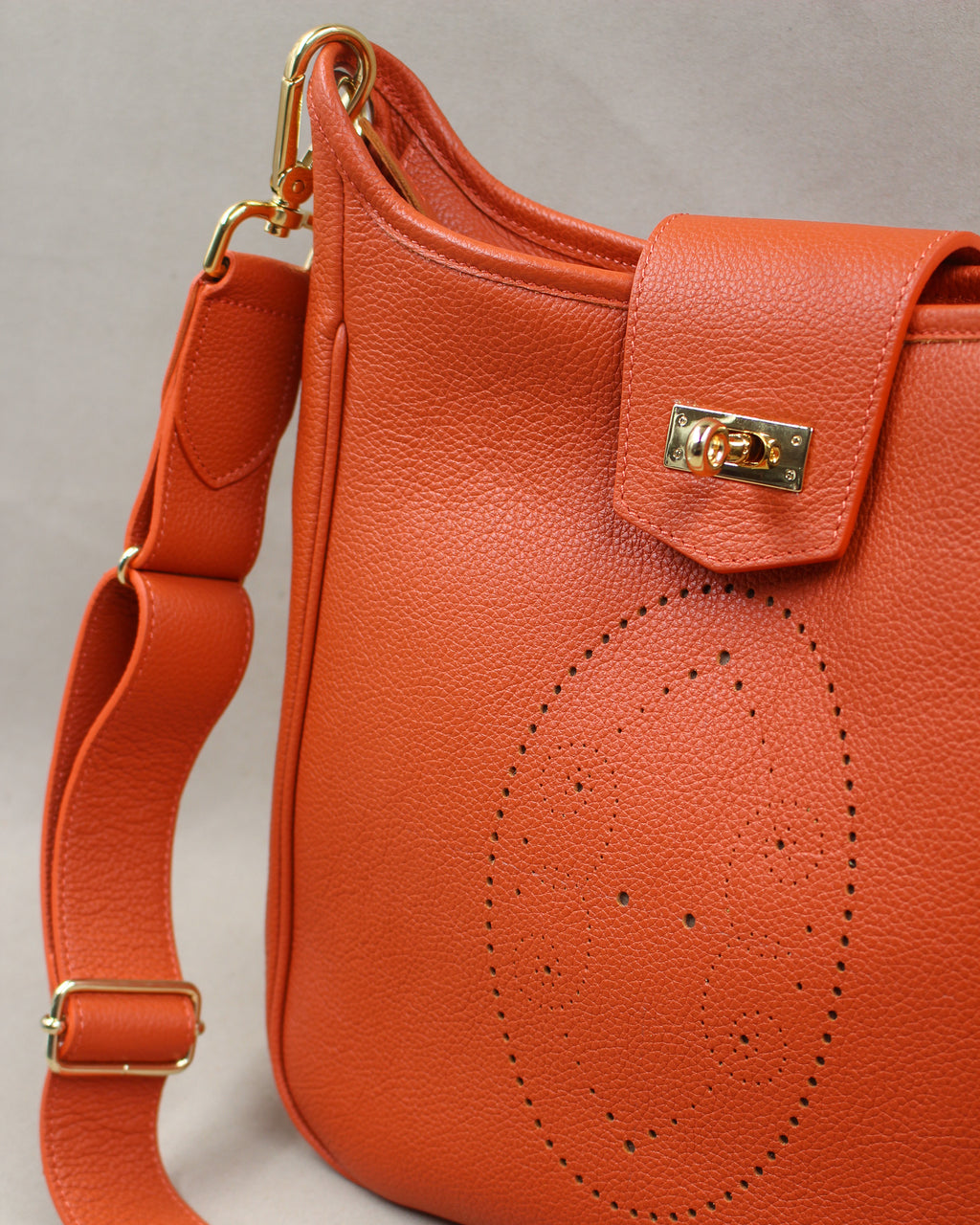 Détail du sac Trianon grand format en cuir orange : motif perforé bout fleuri, fermoir tournant doré sur le rabat et large bandoulière réglable à mousqueton doré, savoir-faire artisanal français
