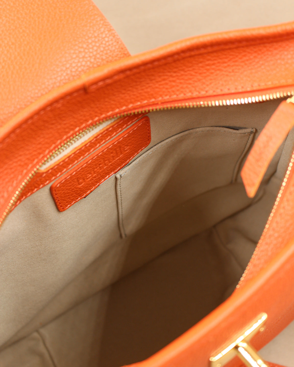 Intérieur du sac Trianon grand format en cuir orange : doublure beige, poche zippée avec tirette en cuir embossée Berthille et poche plaquée