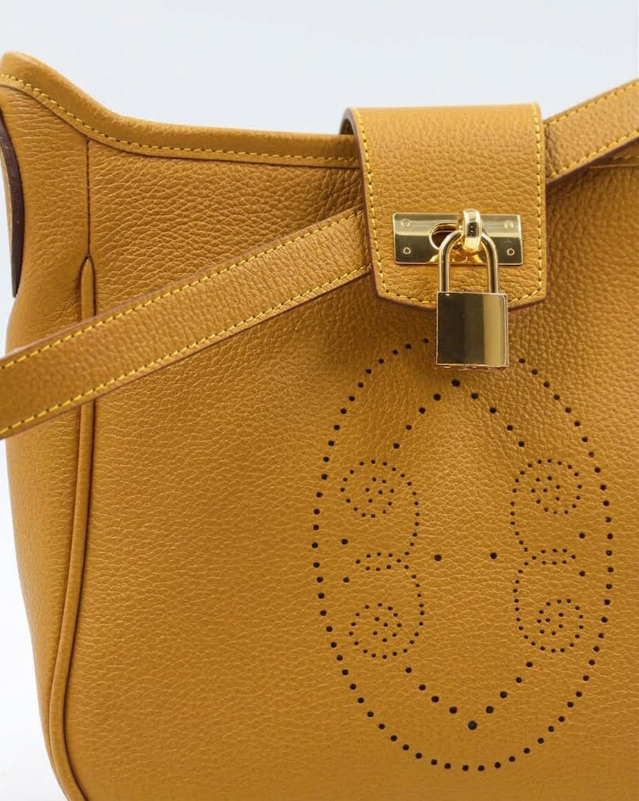 Gros plan sur le motif perforé bout fleuri du sac Trianon en cuir jaune moutarde grainé, cadenas doré et coutures sellier, savoir-faire artisanal français
